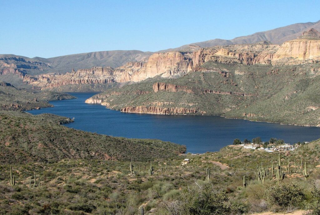 Apache Lake winding between layered red and tan canyon walls, with saguaros and green desert slopes in the foreground