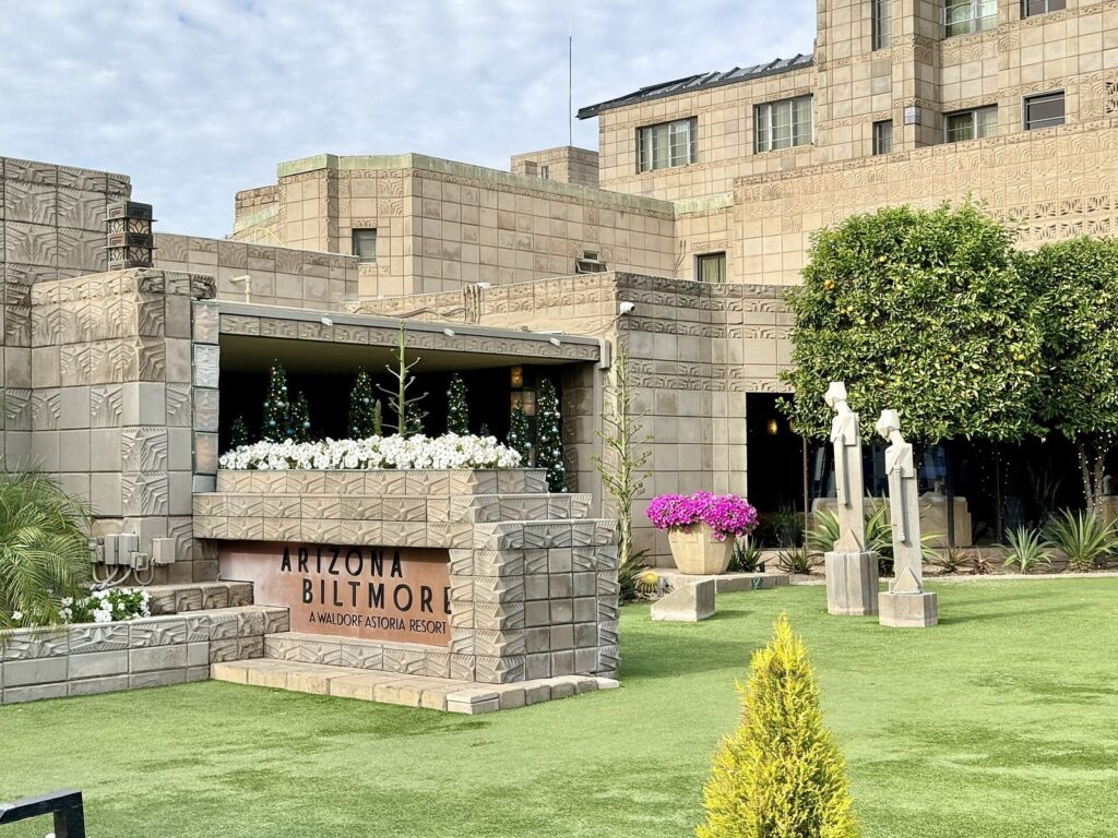 The patterned concrete-block entrance of the Arizona Biltmore, one of the best resorts in Phoenix, with a lawn, white flowers and slender sculptures in front