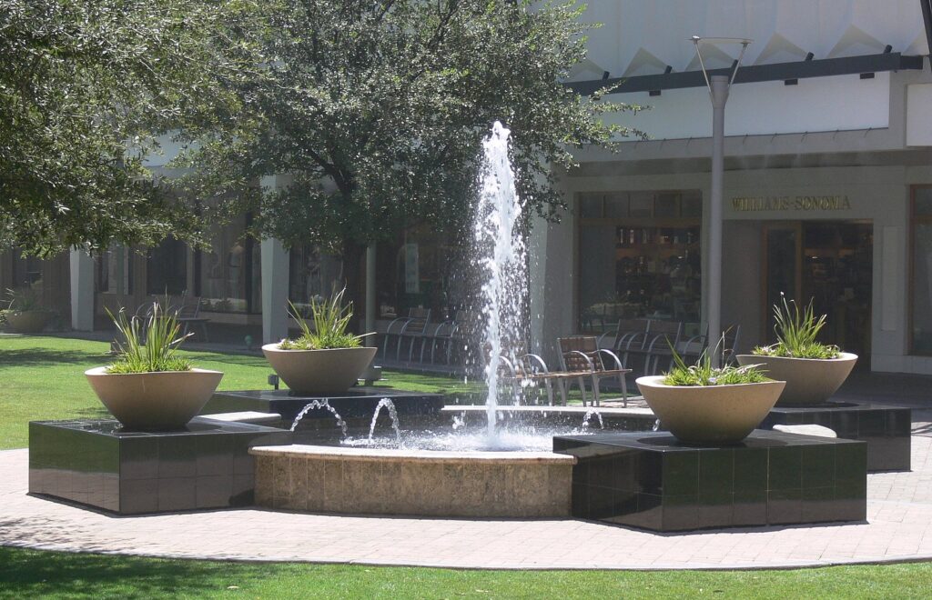 A fountain splashing among planters and lawn in a courtyard at Biltmore Fashion Park, the city's best open-air center for shopping in Phoenix
