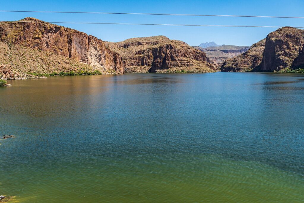Canyon Lake's blue-green water between tall red and tan cliffs, with distant peaks on the horizon under a blue sky