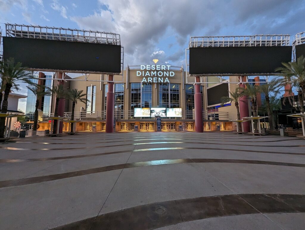 The illuminated entrance of Desert Diamond Arena in Glendale at dusk, framed by palm trees