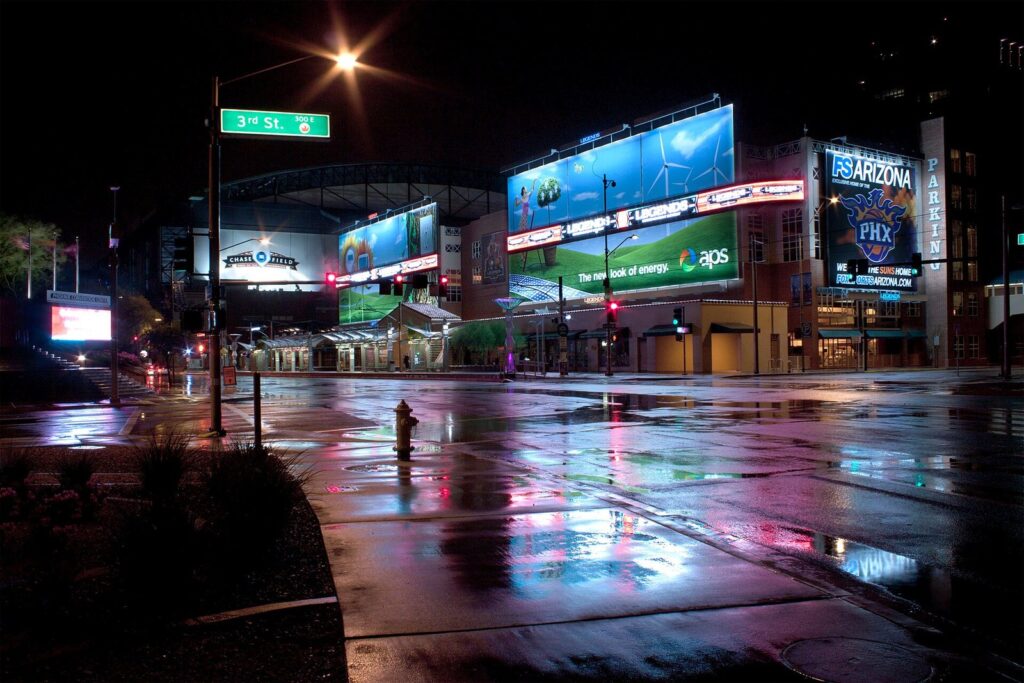 Rain-soaked streets reflecting billboards and streetlights near Chase Field in downtown Phoenix at night