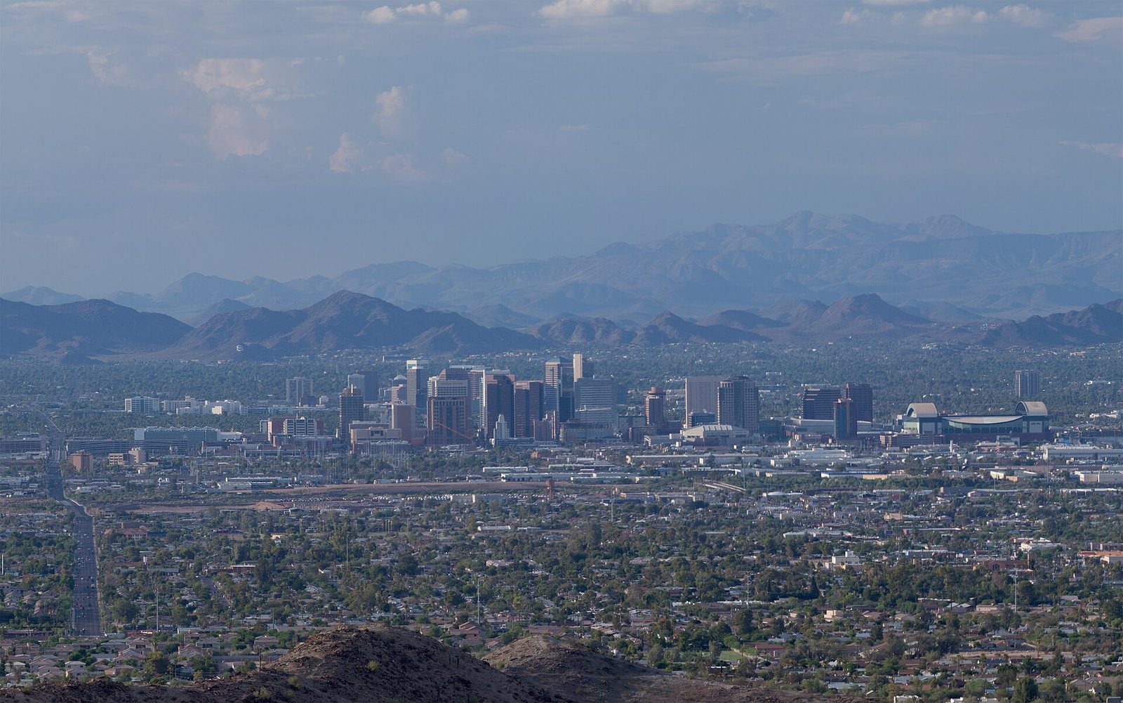 Downtown Phoenix's high-rises and the domed Chase Field seen from South Mountain, with the Phoenix Mountains and distant ranges behind