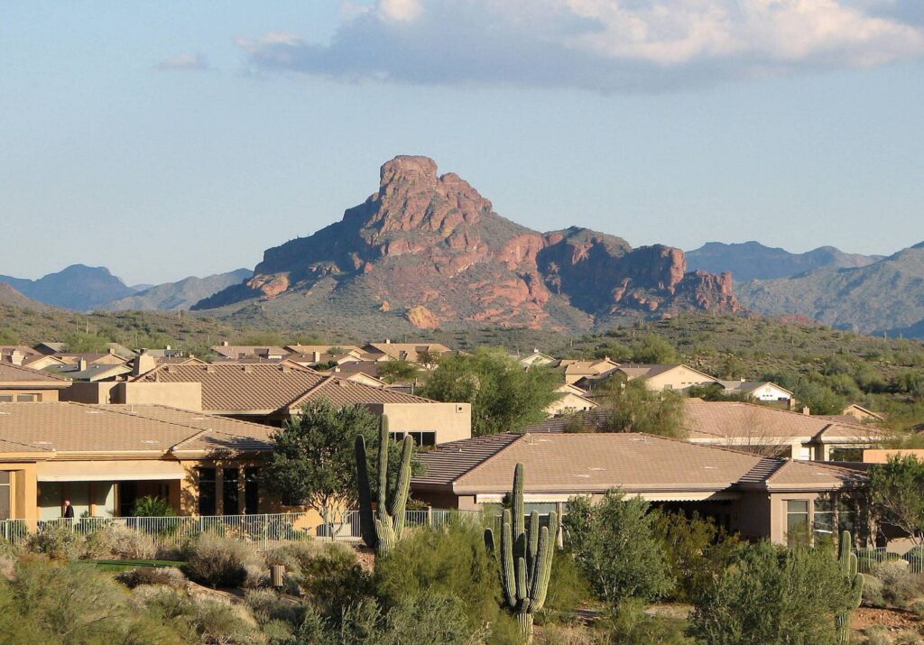 Tile-roofed homes and saguaros below a craggy red mountain in Fountain Hills, Arizona, under a partly cloudy sky