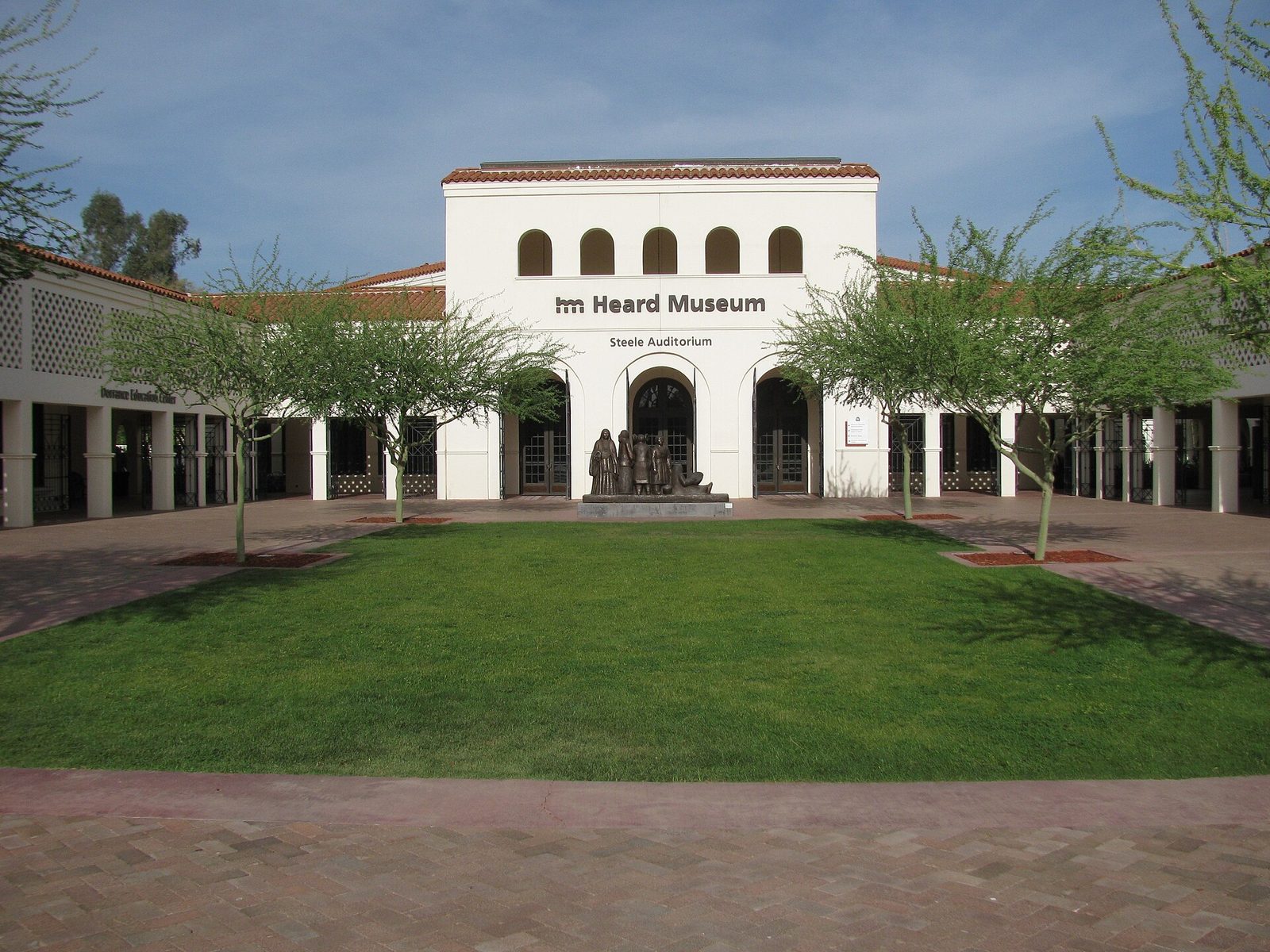 The Heard Museum's white arched entrance building behind a lawn and brick courtyard on a sunny day