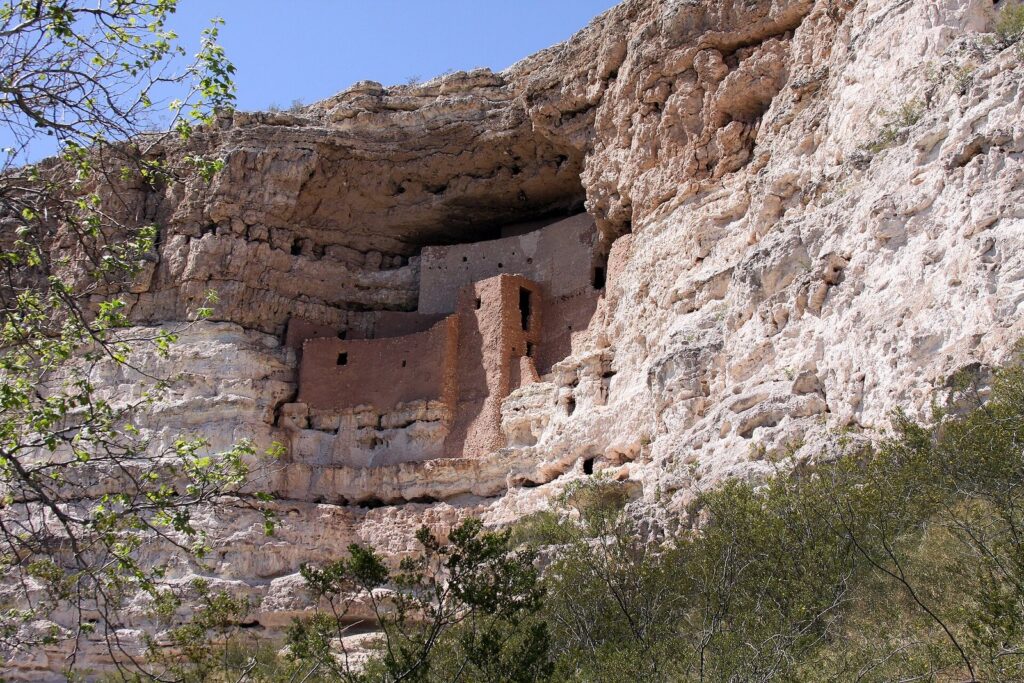Montezuma Castle's multistory adobe cliff dwelling tucked into a pale limestone alcove high on a cliff, framed by green leaves