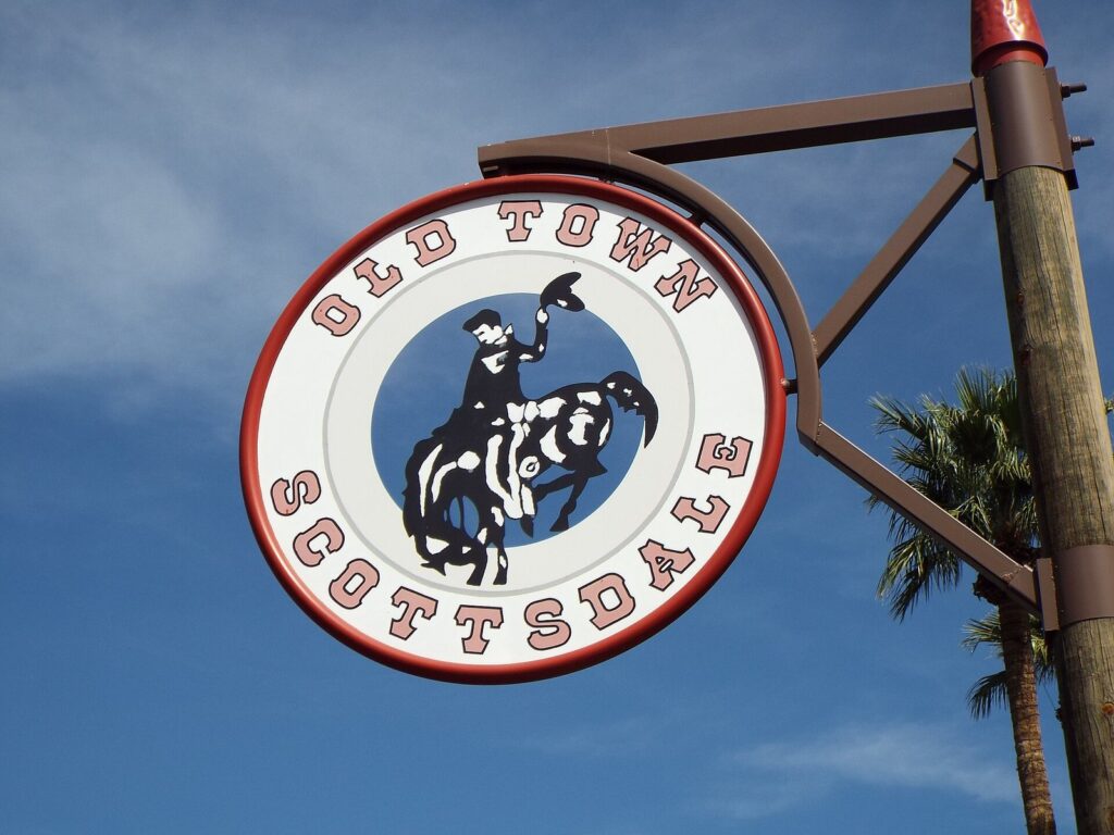 The round Old Town Scottsdale sign with a bucking-horse rider hanging from a wooden post