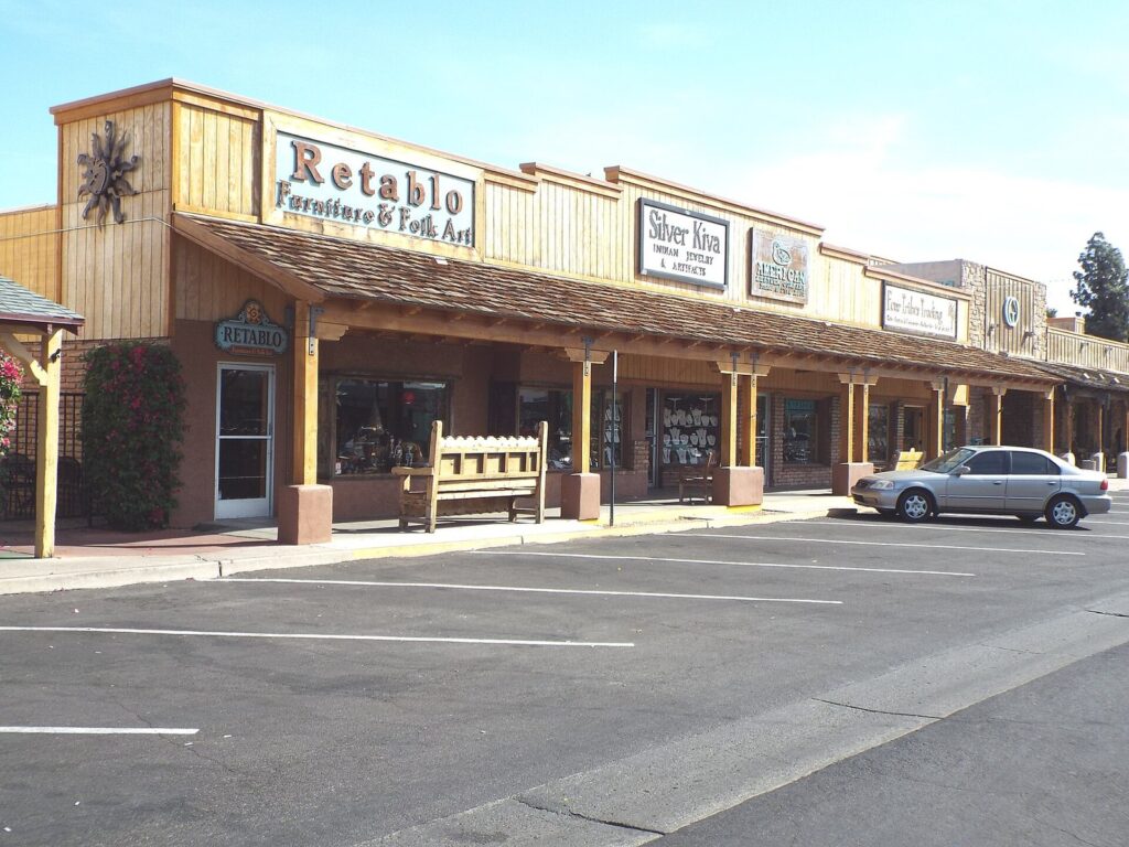 Western-style storefronts with a covered wooden walkway and parking spaces on a sunny street in Old Town Scottsdale