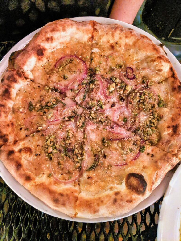 A whole wood-fired pizza topped with thin slices of red onion and chopped pistachios at Pizzeria Bianco, a fixture on any list of the best restaurants in Phoenix