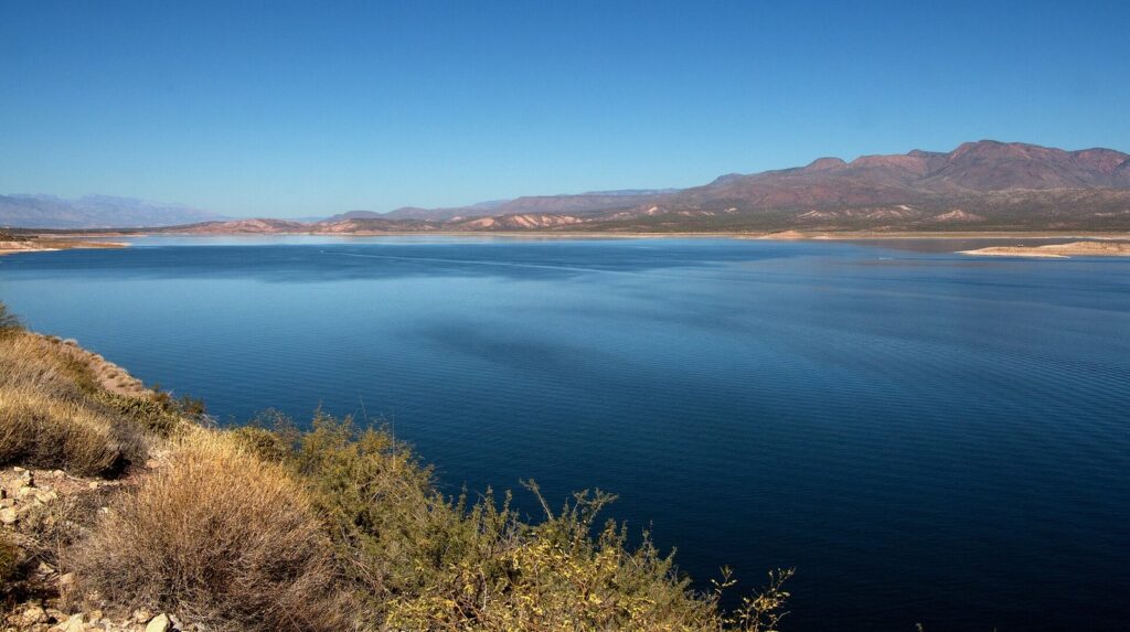 The wide blue expanse of Roosevelt Lake stretching to distant mountains, seen from a desert hillside