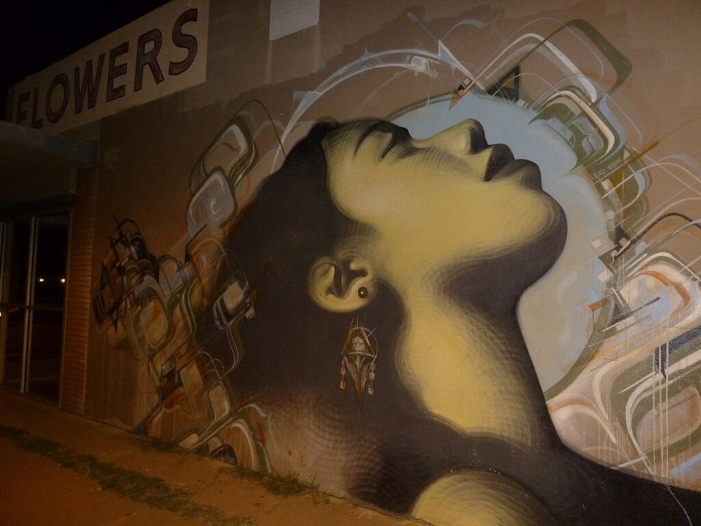 A large mural of a woman's face painted on the side of a building along Roosevelt Row in downtown Phoenix at night