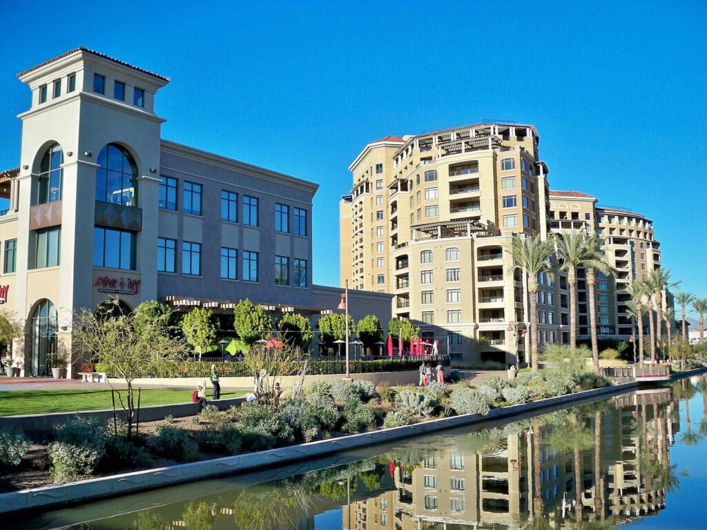Shops and condominium towers reflected in the canal at the Scottsdale Waterfront under a clear blue sky