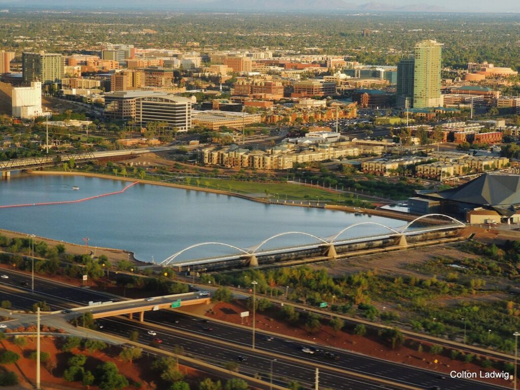 Aerial view of Tempe Town Lake with downtown Tempe and Arizona State University buildings beyond and a freeway in the foreground
