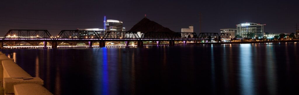Tempe Town Lake at night, with the lights of the rail bridge and Tempe buildings reflected in the dark water