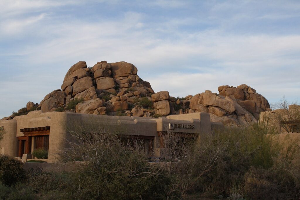 Adobe-style buildings of The Boulders resort in Carefree below a pile of giant rounded granite boulders under a pale blue sky