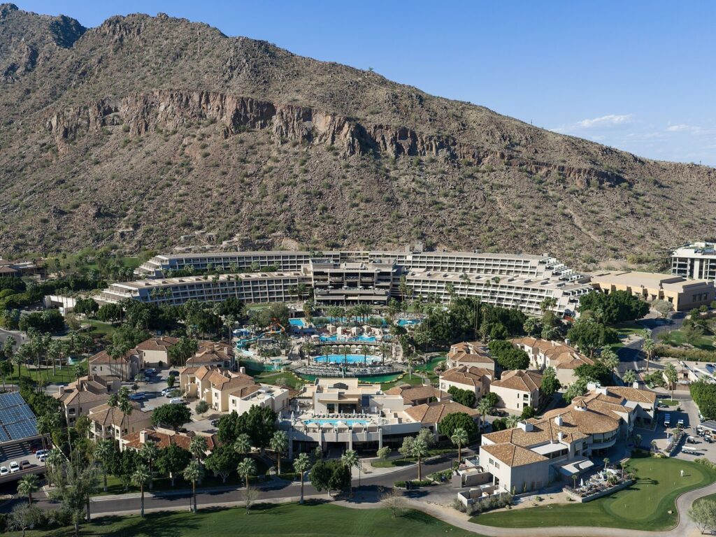 An aerial view of The Phoenician resort in Scottsdale, its terraced main building and pools spread below the rocky slope of Camelback Mountain