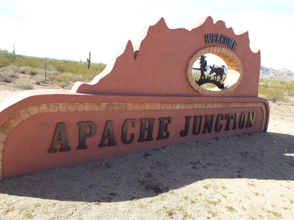 The red-rock welcome sign for Apache Junction with desert scrub and the Superstition Mountains in the distance