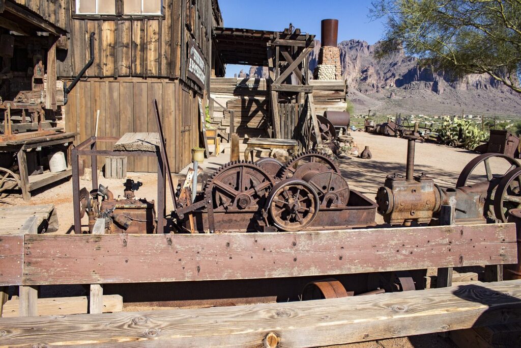 Rusted mining machinery and weathered wooden buildings at Goldfield Ghost Town with the Superstition Mountains behind