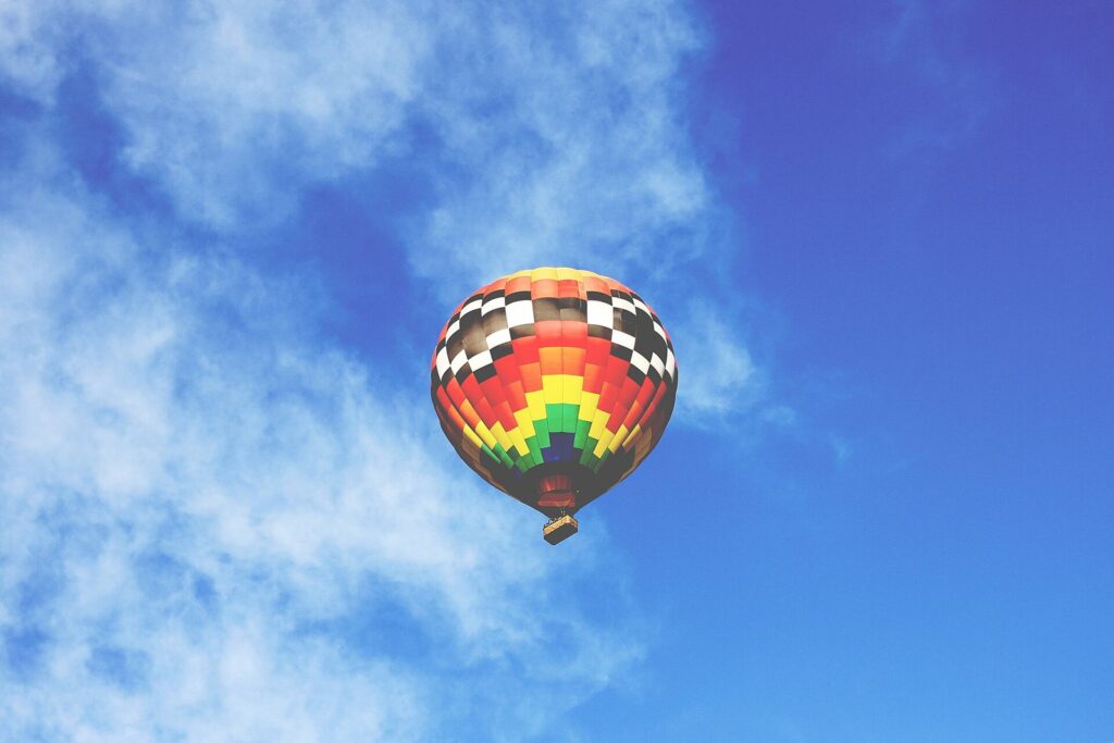 A rainbow-striped hot air balloon floating in a blue sky over Phoenix