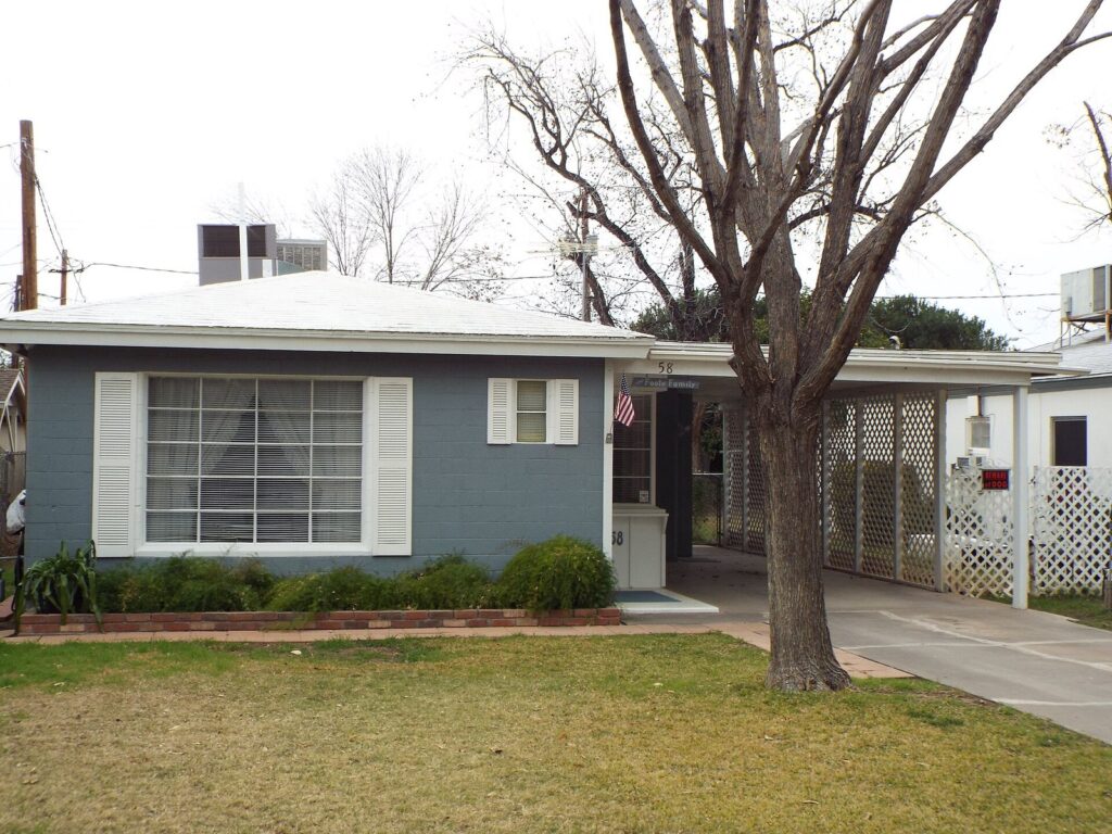 A small 1950s house with a white roof and bare winter tree on a quiet street in Mesa