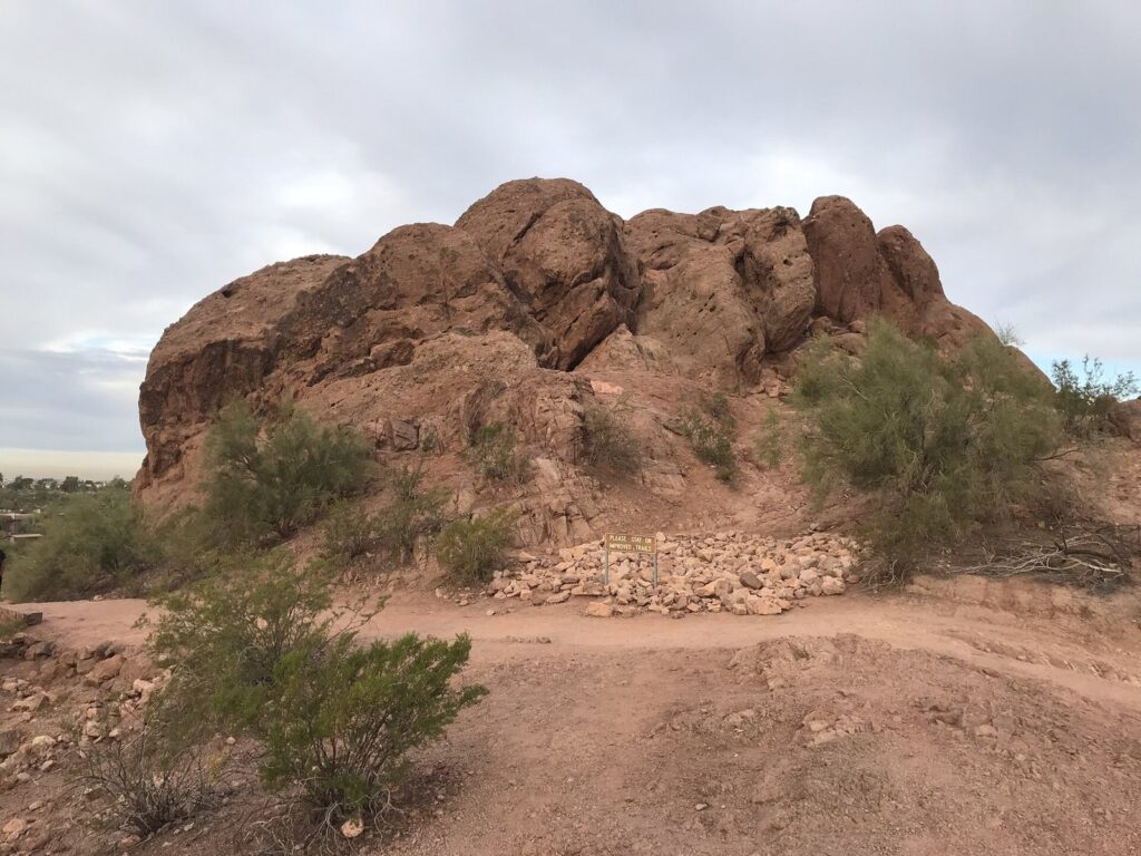 A red sandstone butte and desert shrubs along a dirt trail in Papago Park under a cloudy November sky