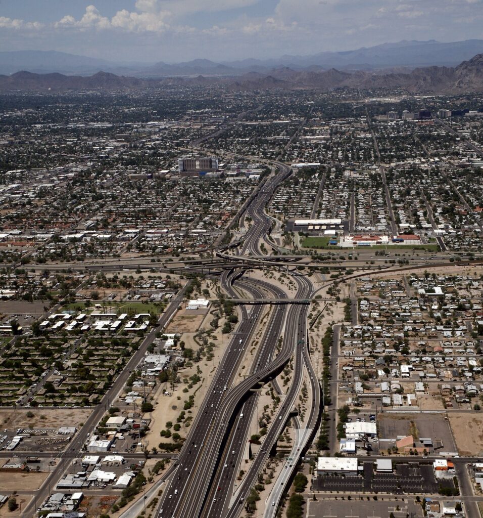 An aerial view of a large freeway interchange cutting through the Phoenix street grid with mountains on the horizon
