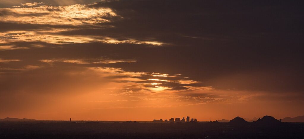 The downtown Phoenix skyline silhouetted against an orange sunset sky with mountains on the horizon
