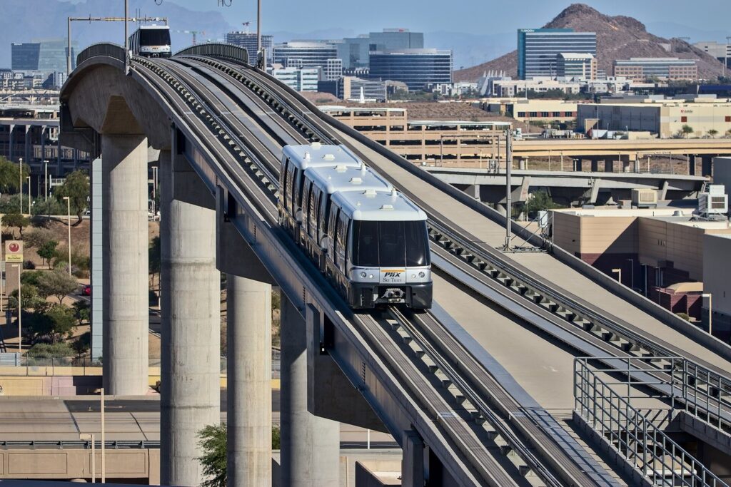 A PHX Sky Train car crossing an elevated guideway with office buildings and a desert butte behind