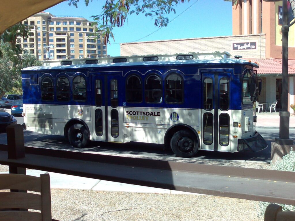 A blue-and-white Scottsdale trolley bus parked at a stop beside a low building